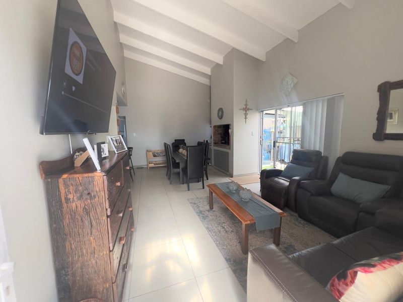 Spacious open-plan living and dining area featuring vaulted ceilings with exposed beams, tiled flooring, and a built-in fireplace with access to the patio.