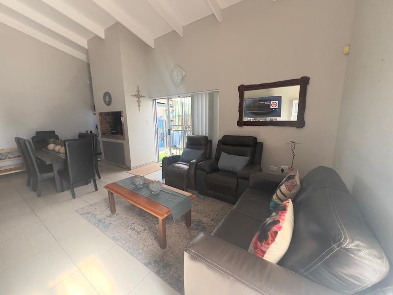 Spacious open-plan living and dining area featuring vaulted ceilings with exposed beams, tiled flooring, and a built-in fireplace with direct access to the patio.