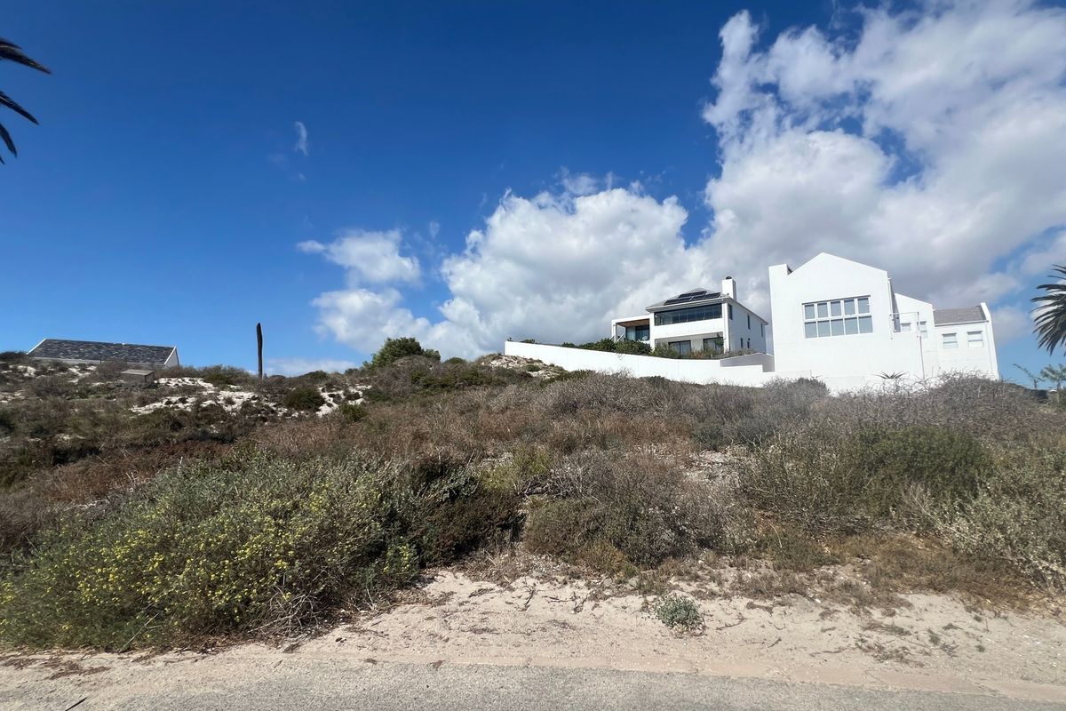 A view of a residential property situated on a sloped, undeveloped coastal plot with native vegetation and a white exterior facade.