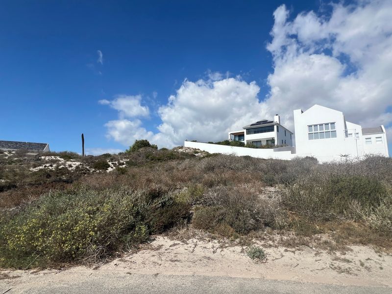 A view of a residential property situated on a sloped, undeveloped coastal plot with native vegetation and a white exterior facade.
