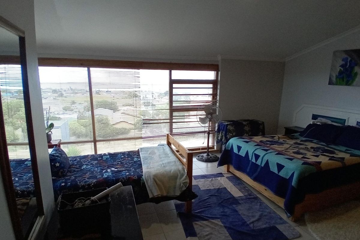 Spacious bedroom featuring large windows with horizontal blinds, tiled flooring, and coved ceiling details, offering ample natural light.