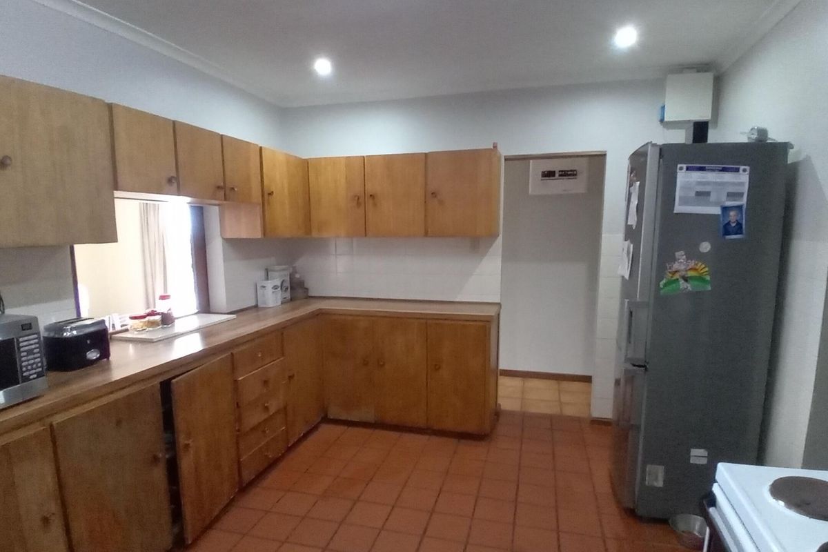 A functional kitchen featuring wooden cabinetry, tiled flooring, and a tiled splashback, offering a classic layout with potential for modern updates.