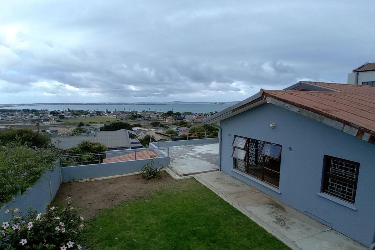Rear exterior view of the property featuring a concrete patio, lawn area, and elevated views over the surrounding neighbourhood and coastline.