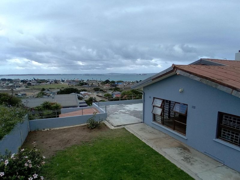 Rear exterior view of the property featuring a concrete patio, lawn area, and elevated views over the surrounding neighbourhood and coastline.