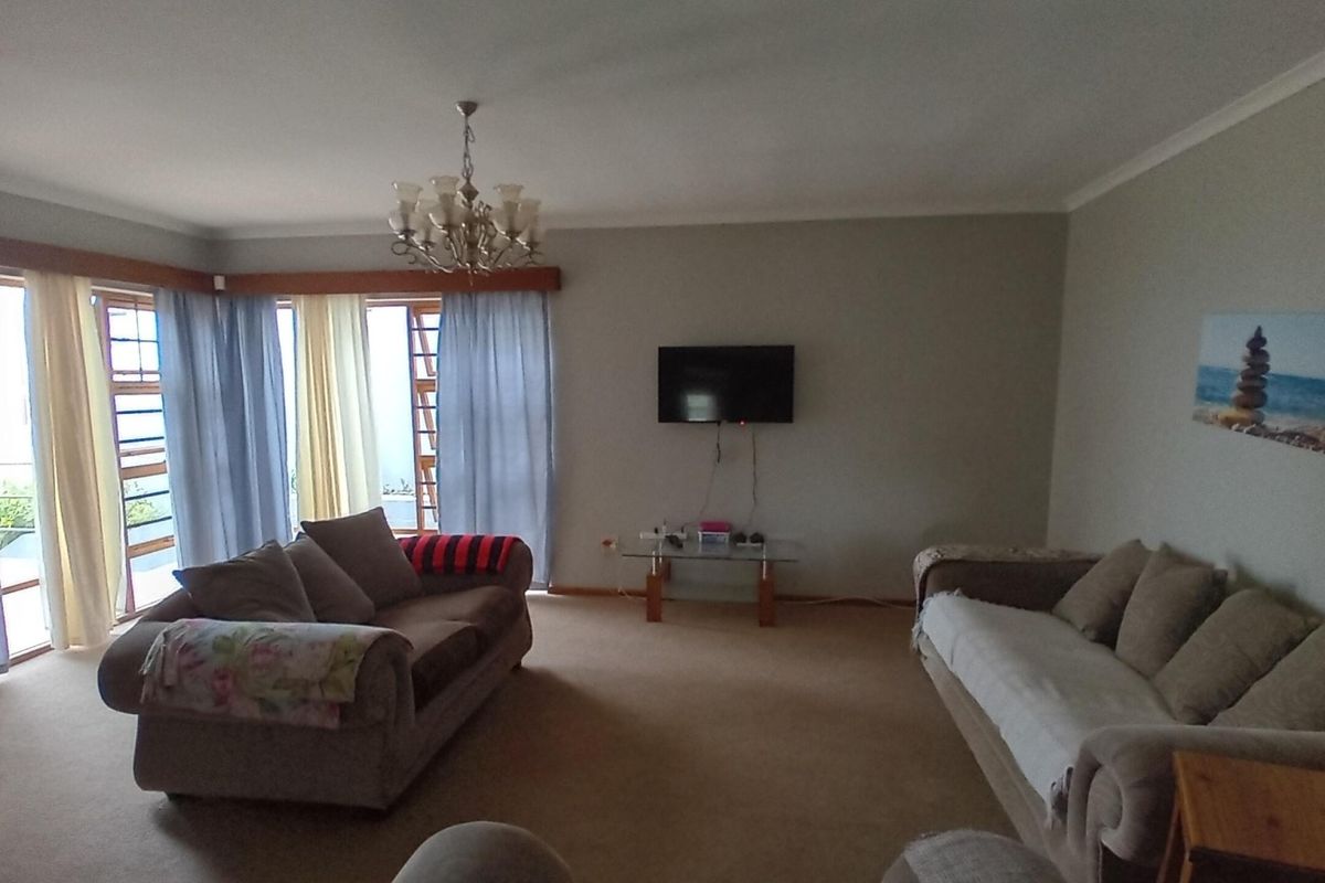 A spacious living room featuring large windows, neutral wall tones, and carpeted flooring, offering a comfortable and functional layout for relaxation.