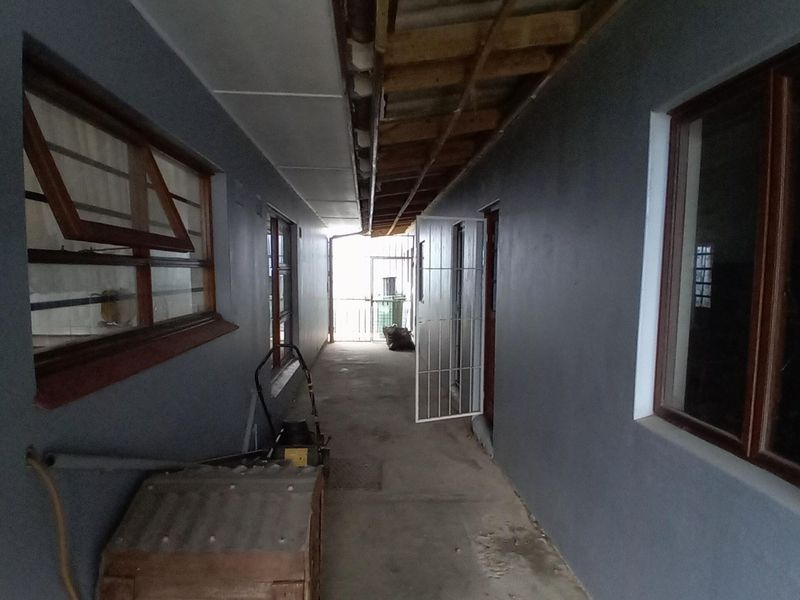 An exterior-facing hallway or walkway featuring concrete flooring, timber-framed windows, and an unfinished ceiling with exposed rafters.