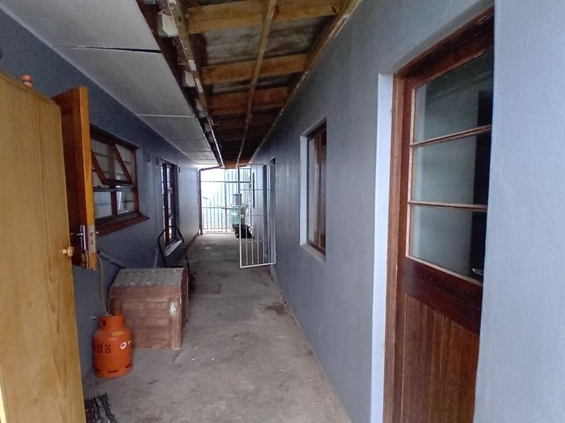 A narrow utility corridor or covered walkway featuring exposed timber rafters, concrete flooring, and access to multiple entry points.