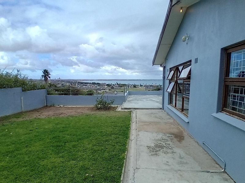 Rear exterior view featuring a concrete patio, lawn area, and perimeter wall with views of the surrounding landscape.