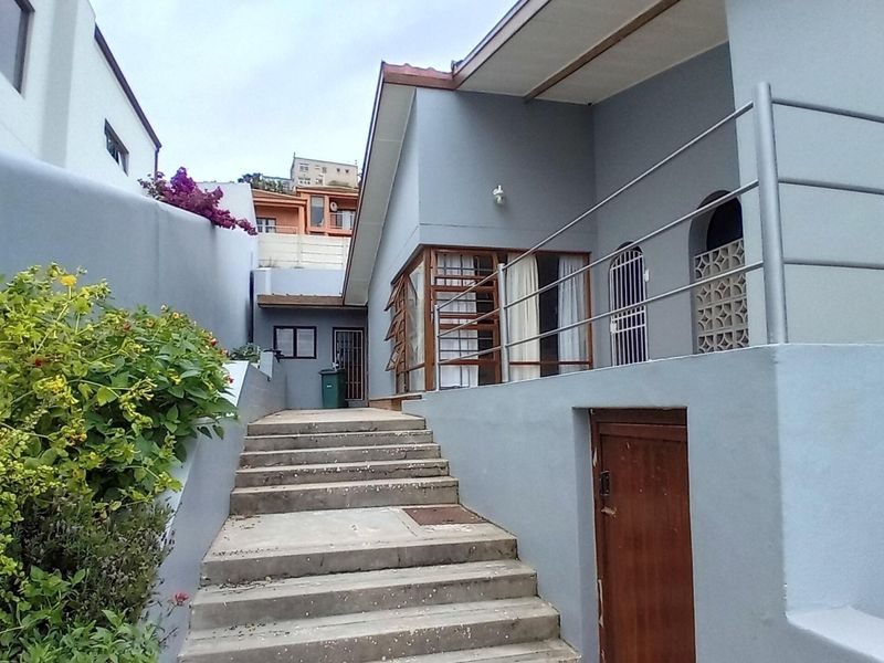 Rear exterior view of the property featuring a concrete staircase leading to a raised patio area with metal railings and security features.