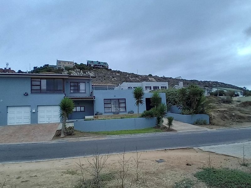 Front elevation of a two-story residential property featuring a double garage, paved driveway, and low-maintenance retaining walls in a hillside setting.