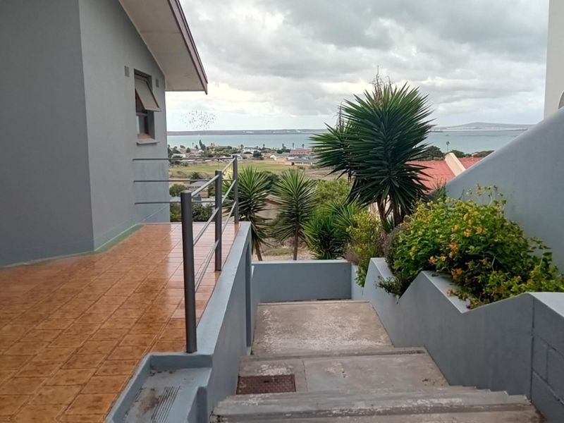An outdoor rear patio area with tiled flooring, metal railings, and concrete stairs leading down, offering a scenic coastal view.
