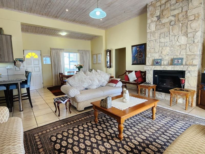 Spacious open-plan living area featuring a prominent stone fireplace, timber-paneled ceilings, tiled floors, and an integrated kitchen with granite countertops.