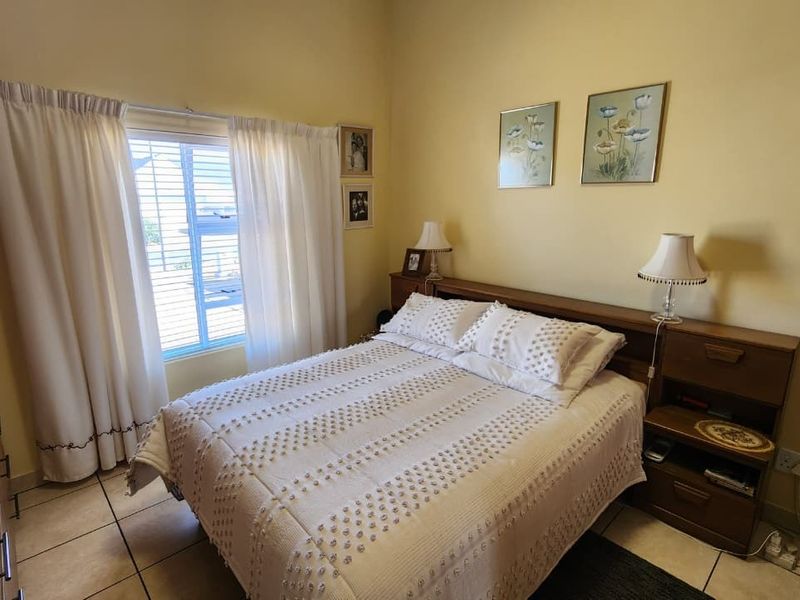 A functional bedroom featuring tiled flooring, a built-in wardrobe, and a window with blinds, offering a comfortable and practical living space.