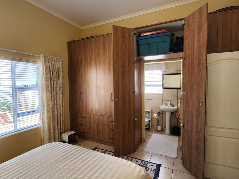Bedroom featuring built-in wooden cupboards and an integrated en-suite bathroom with a pedestal basin and tiled flooring.