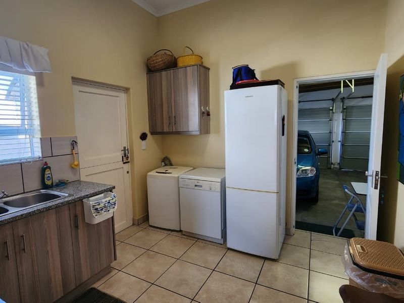 Functional scullery area featuring double stainless steel sink, granite countertops, laminate cabinetry, and tiled flooring, with direct access to the garage.