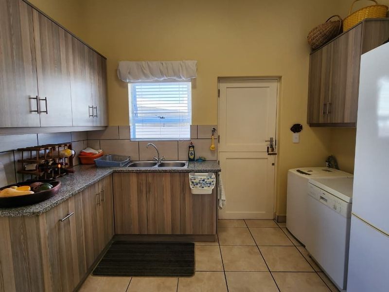 Functional laundry room featuring wood-look cabinetry, granite countertops, a double basin sink, and tiled flooring with direct access to the exterior.
