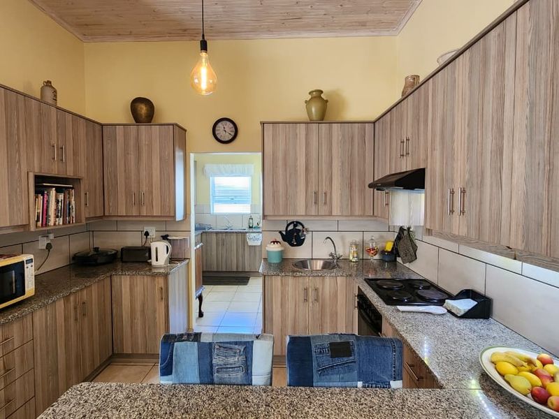 A functional kitchen featuring wood-look cabinetry, granite countertops, a tiled backsplash, and a timber ceiling, with an adjacent scullery area visible.