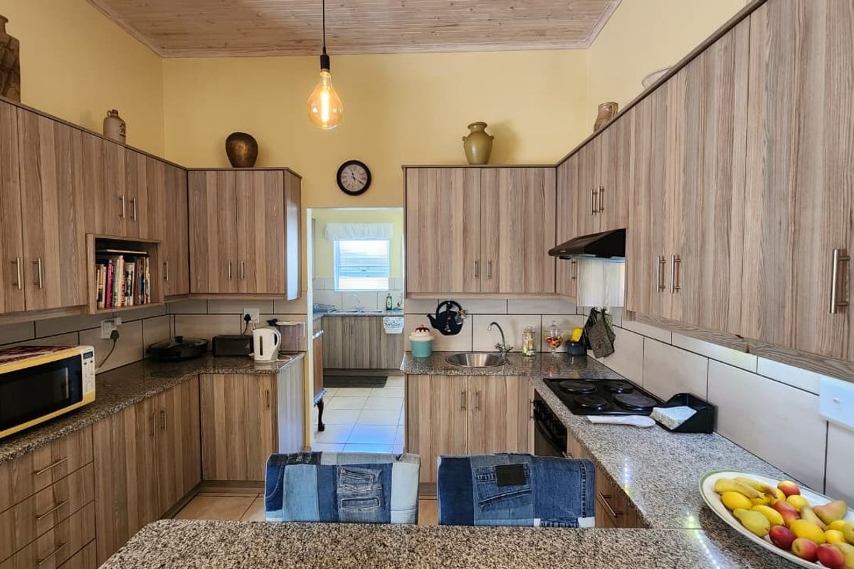 A functional kitchen featuring wood-look cabinetry, granite countertops, a tiled backsplash, and a timber ceiling, with an adjacent scullery area visible.