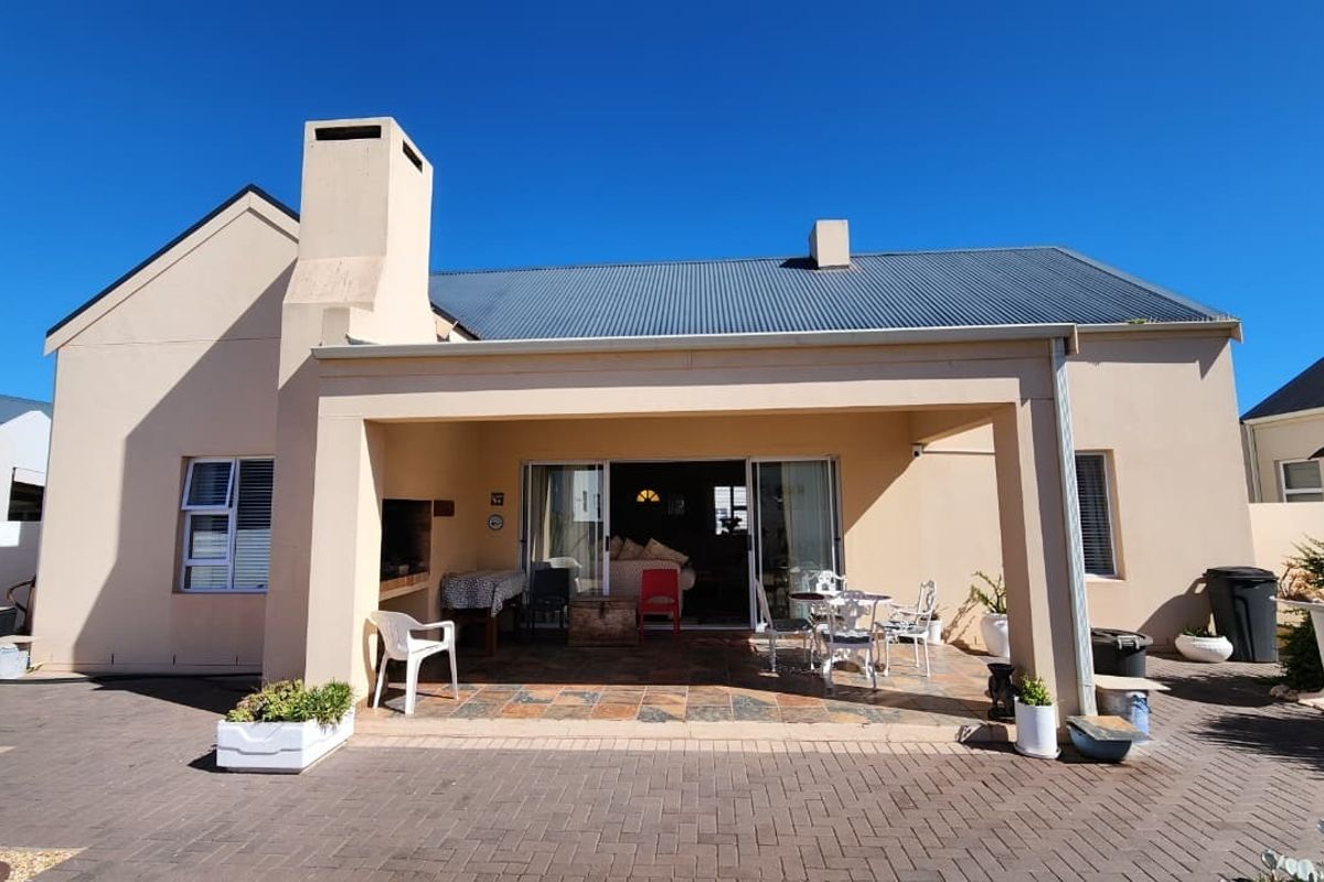 Rear view of the property featuring a covered patio with a built-in braai, paved courtyard area, and direct access to the interior via sliding doors.
