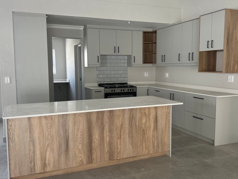 Modern kitchen featuring light grey cabinetry, wood-tone accents, a central island, stone countertops, and a subway tile backsplash with a gas stove.