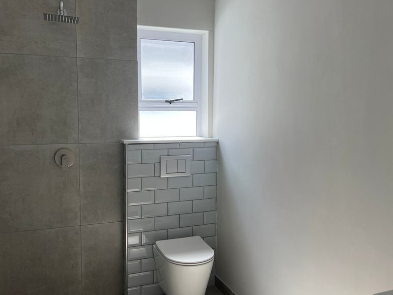 Modern bathroom featuring a walk-in shower with a rain shower head, wall-mounted toilet with concealed cistern, and contemporary grey tiling.