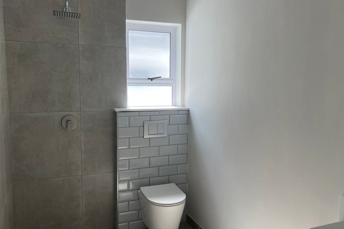Modern bathroom featuring a walk-in shower with a rain shower head, wall-mounted toilet with concealed cistern, and contemporary grey tiling.