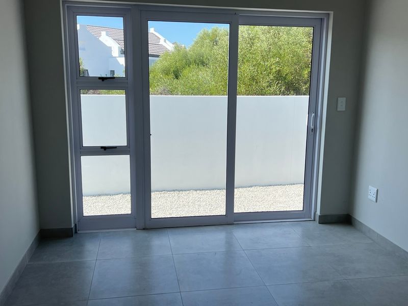 A bright, empty living area featuring modern tiled flooring and a large sliding glass door providing access to an outdoor space.