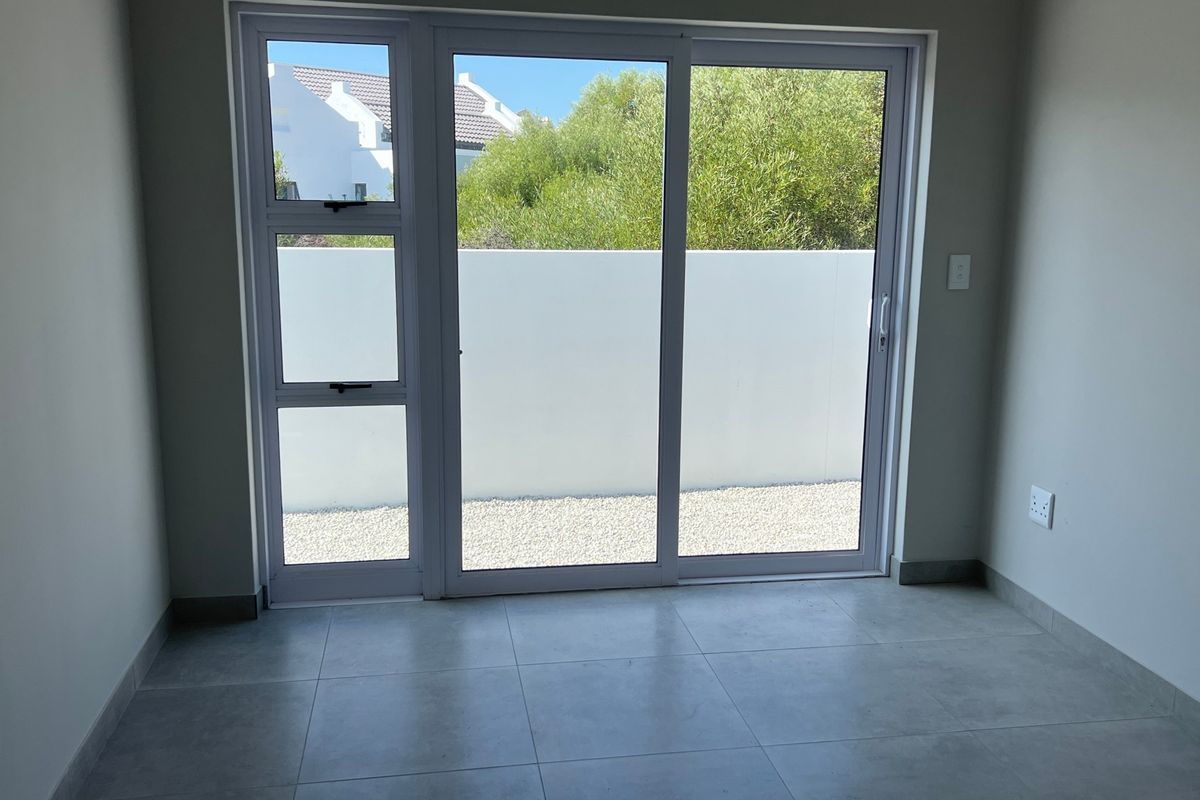 A bright, empty living area featuring modern tiled flooring and a large sliding glass door providing access to an outdoor space.