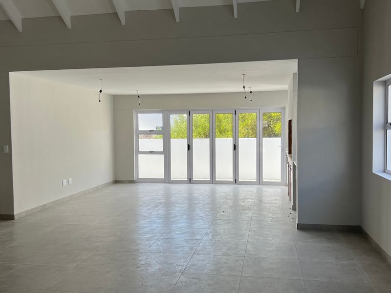 Spacious open-plan living area featuring neutral tiled flooring, exposed beam ceilings, and large bi-fold doors providing ample natural light and garden access.