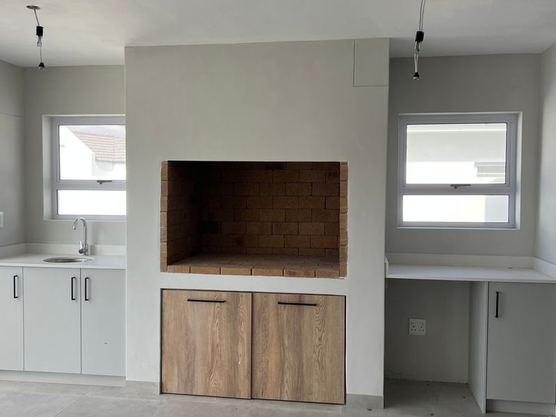 A modern, empty covered patio area featuring a built-in brick braai, sink, and clean cabinetry, ready for outdoor entertaining.