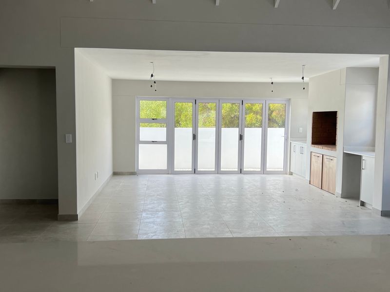 Spacious open-plan living area featuring tiled floors, built-in braai, and large bi-fold doors providing seamless access to the outdoor space.