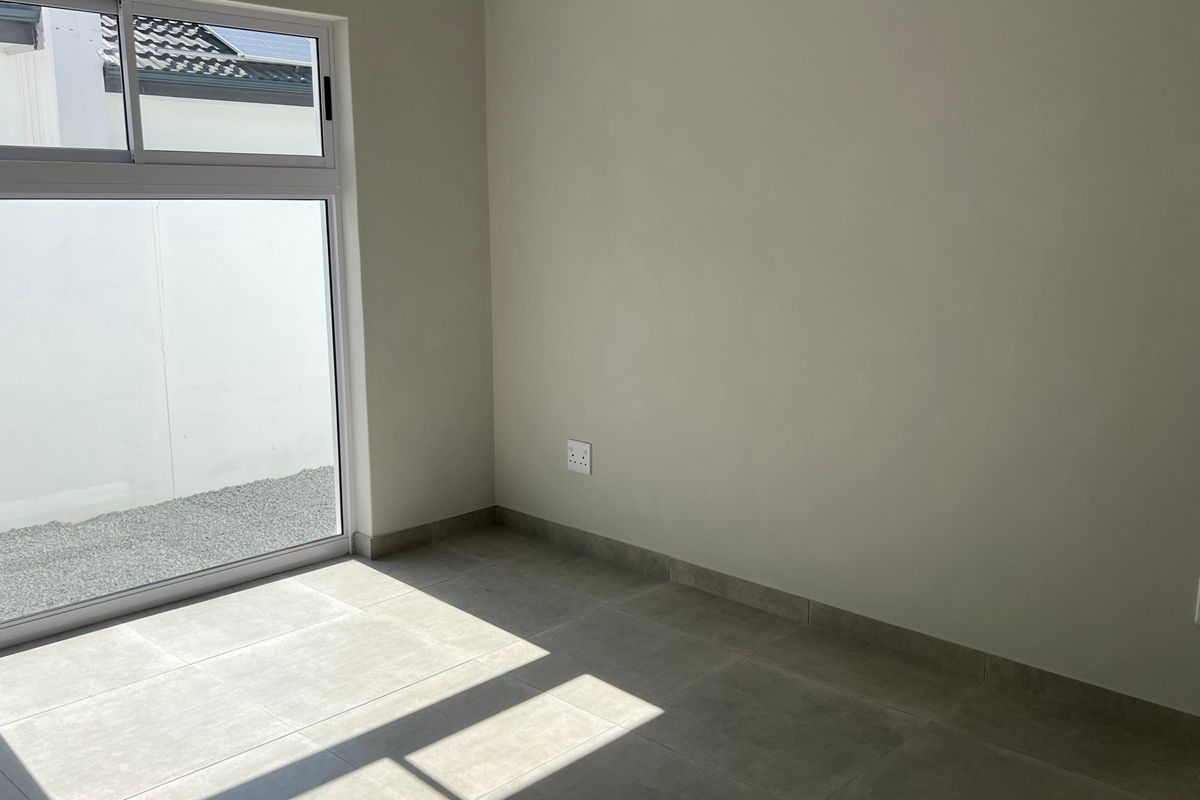 A bright, empty bedroom featuring neutral tiled flooring, modern skirting boards, and a large sliding glass door providing natural light and outdoor access.