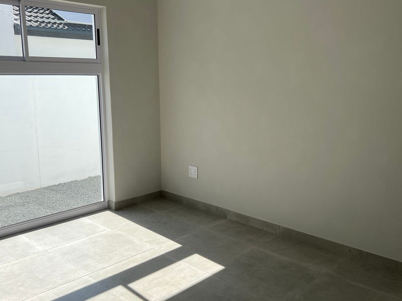 A bright, empty bedroom featuring neutral tiled flooring, modern skirting boards, and a large sliding glass door providing natural light and outdoor access.
