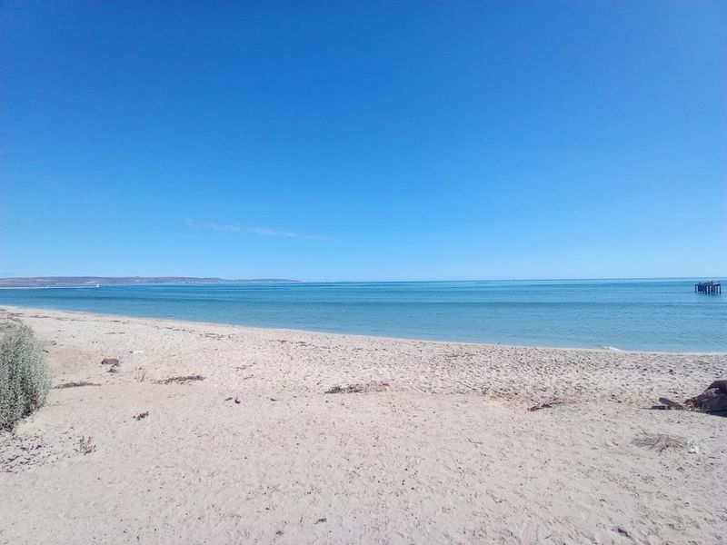 A scenic view of the sandy beach and calm ocean waters under a clear blue sky.