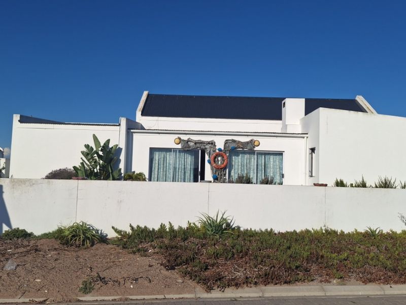 A front view of a white house featuring a metal roof, chimney, and a solid boundary wall with a landscaped verge.