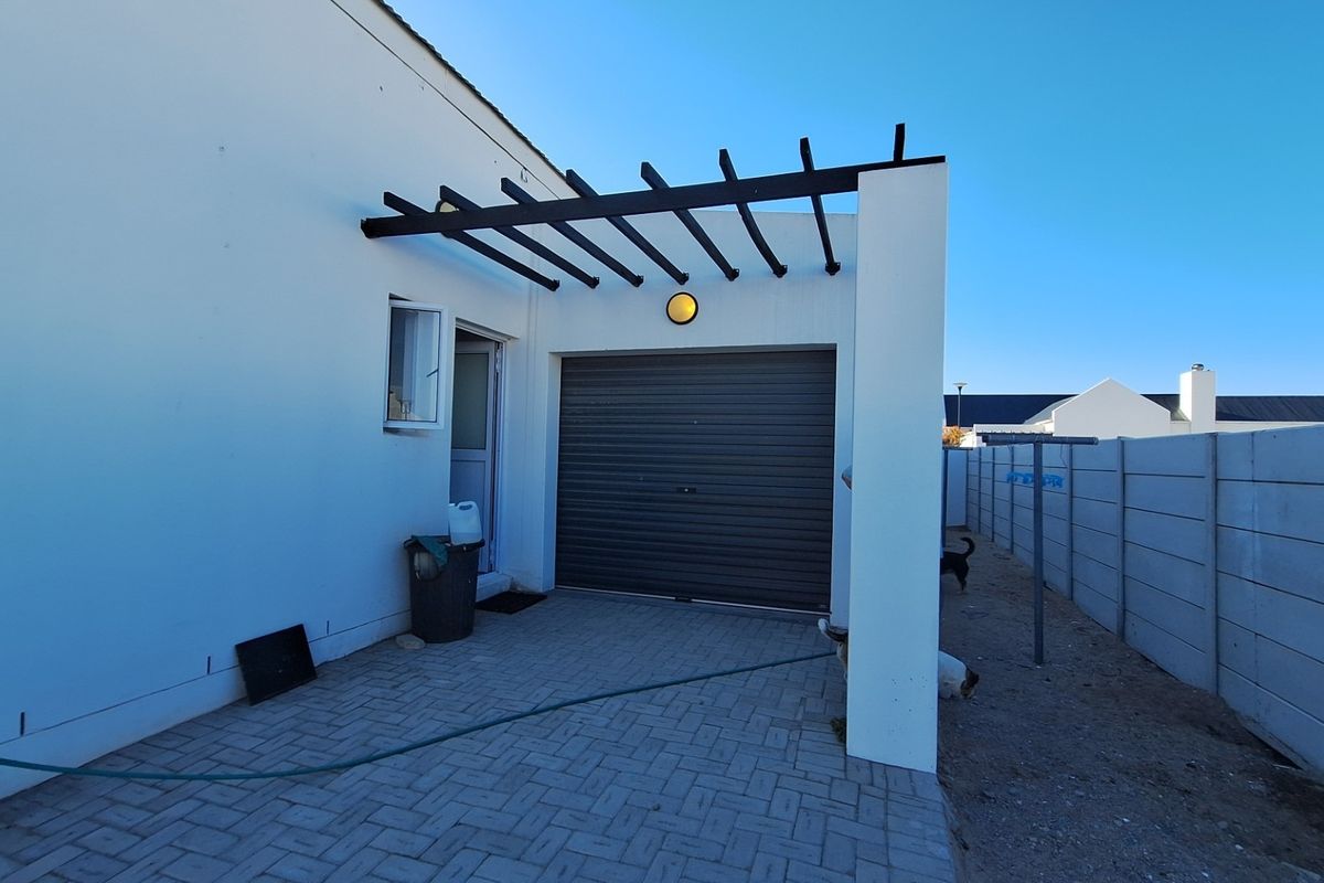 Rear exterior view featuring a paved patio area, a pergola structure, and a single garage door with a surrounding precast concrete boundary wall.