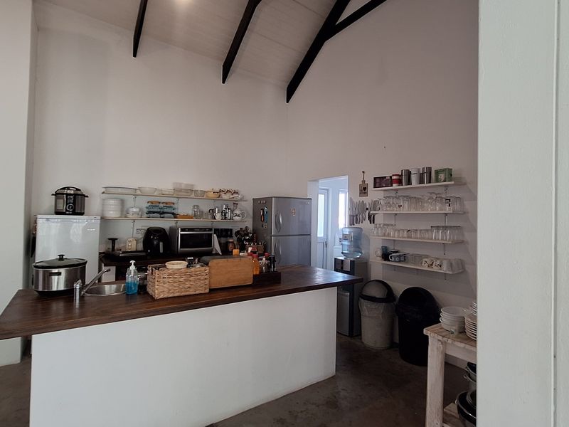 A rustic kitchen area featuring a central island, open shelving, and a high vaulted ceiling with exposed timber beams.