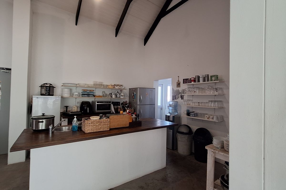 A rustic kitchen area featuring a central island, open shelving, and a high vaulted ceiling with exposed timber beams.