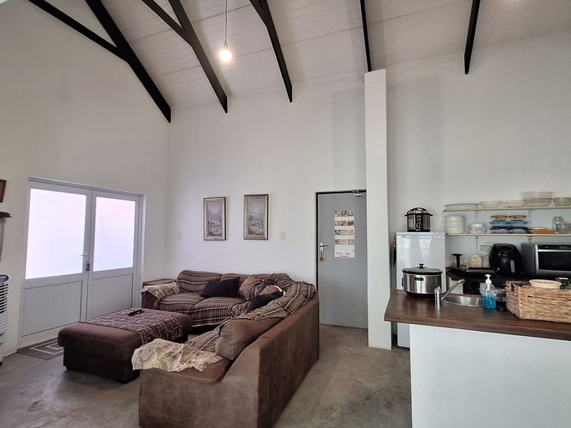 Open-plan living area featuring a high vaulted ceiling with exposed beams, integrated kitchen space with countertop, and direct access to the exterior.