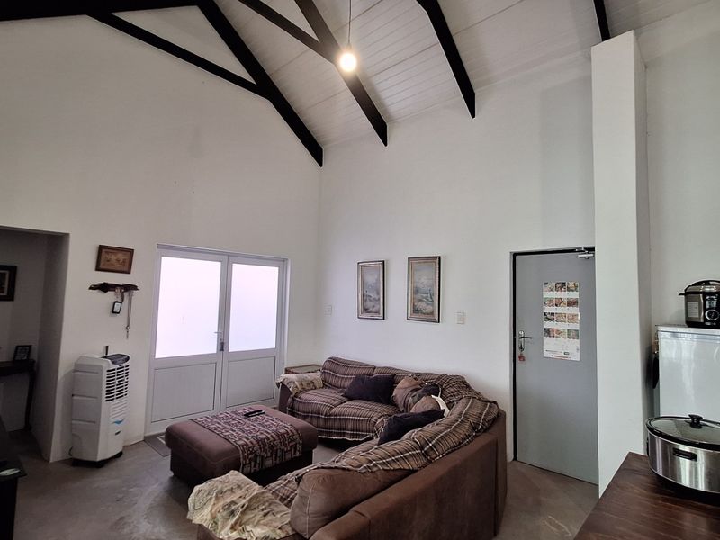 Open plan living area featuring a high vaulted ceiling with exposed timber beams, concrete flooring, and direct access to the exterior via double doors.