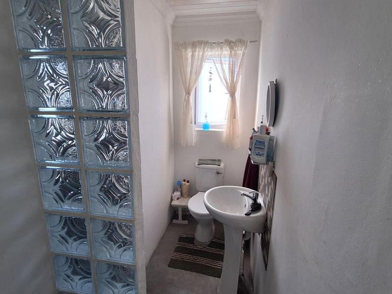 A compact bathroom featuring a pedestal sink, toilet, and a decorative glass block partition wall.