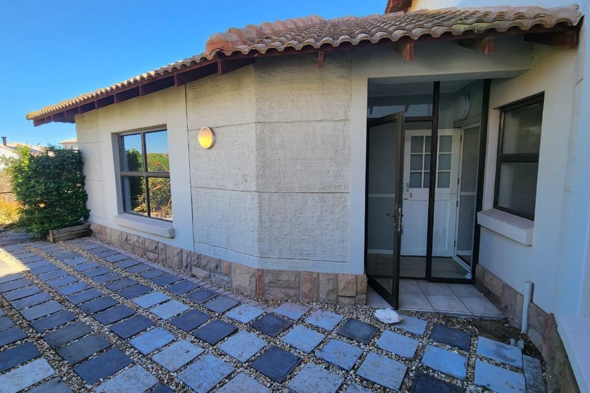 Rear exterior view featuring a paved patio area, stone-clad wall accents, terracotta roof tiles, and aluminium-framed glass door access.