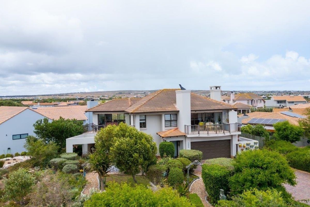 Aerial view of a multi-level residential property featuring a tiled roof, balcony, attached garage, and established landscaped garden in a suburban setting.