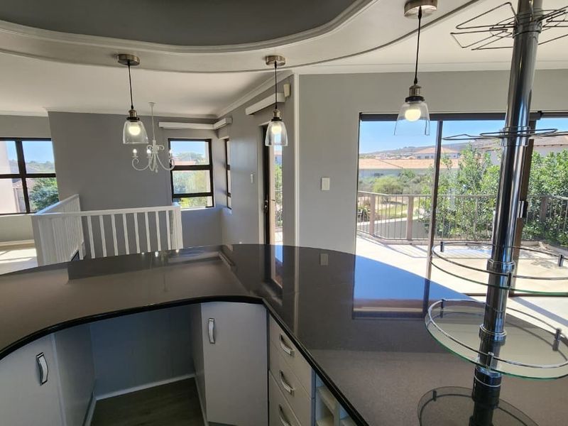 Spacious open-plan living area featuring a large granite kitchen island, modern pendant lighting, and sliding doors leading to a balcony with scenic views.