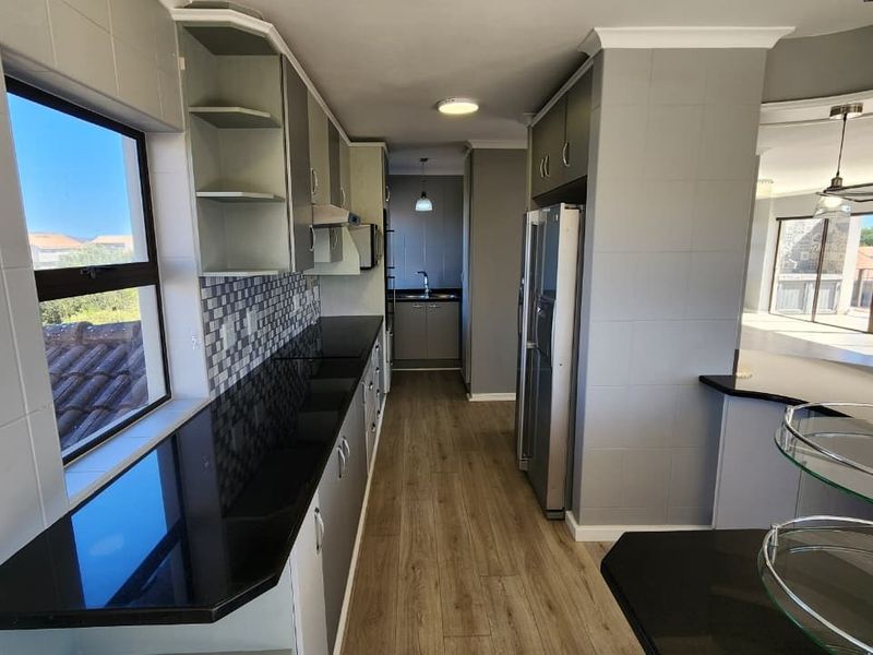 Modern galley-style kitchen featuring sleek granite countertops, mosaic tile backsplash, ample built-in cabinetry, and durable laminate flooring with an adjacent scullery area.