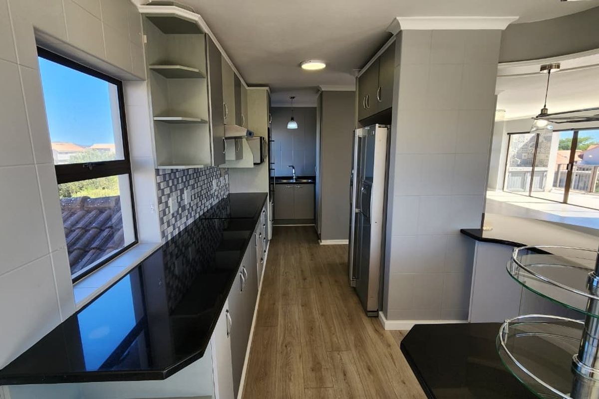 Modern galley-style kitchen featuring sleek granite countertops, mosaic tile backsplash, ample built-in cabinetry, and durable laminate flooring with an adjacent scullery area.