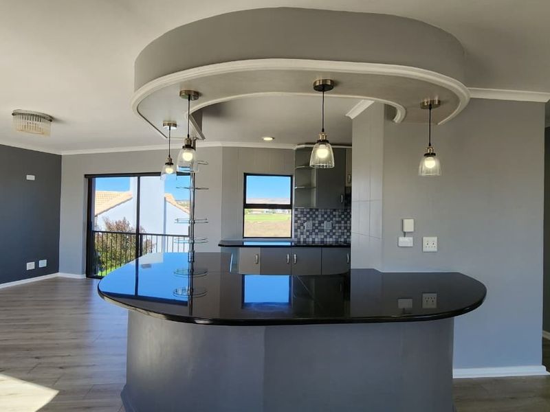 Modern open-plan living area featuring a curved breakfast bar with granite countertop, pendant lighting, and laminate flooring, seamlessly connecting to the kitchen space.