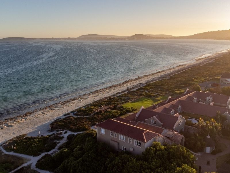 An aerial view of a coastal residential property featuring direct beach access and expansive ocean views at sunset.