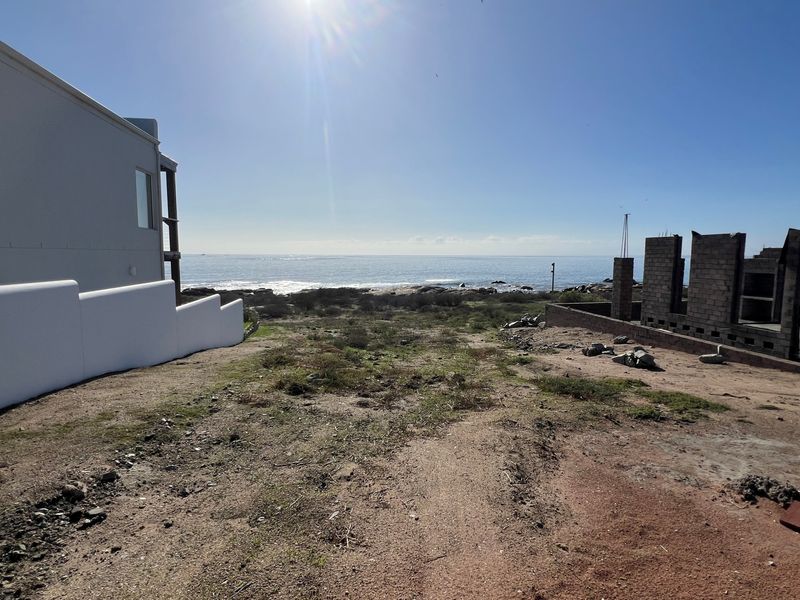 A vacant residential plot featuring direct ocean views, adjacent to existing residential structures and partially completed masonry construction.