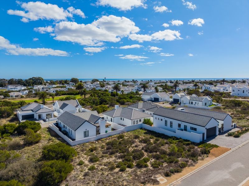 Aerial view of a modern residential estate featuring white homes with pitched roofs, paved driveways, and surrounding coastal landscape.
